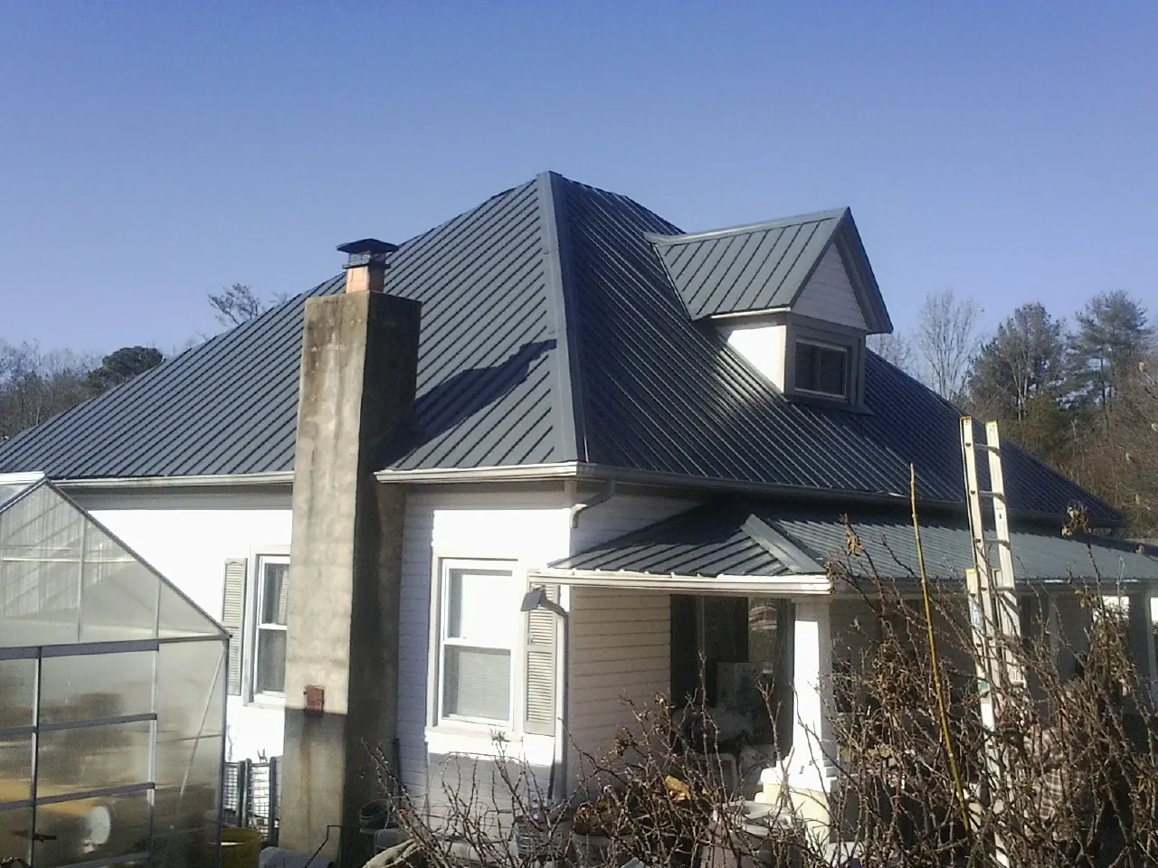 Dark blue standing seam metal roof on a white farmhouse with dormer — Slate & Tile Roof Repair by Roofing Brothers in Jones
