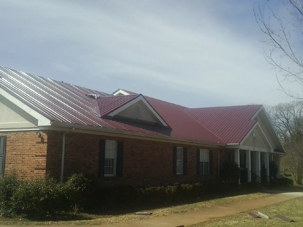 Red metal roof with gabled entries on a long brick building, from a Hail Damage Roof Repair job in Jones