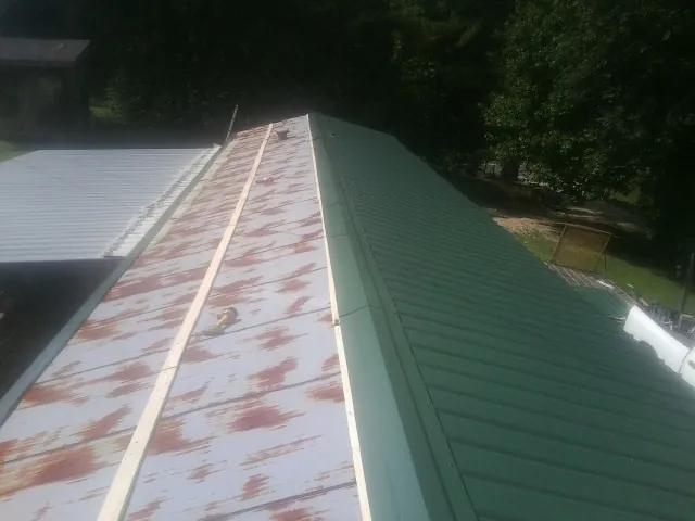 Old rusted panels beside newly installed green metal roofing — Wind Damage Roof Repair by Roofing Brothers in Jones