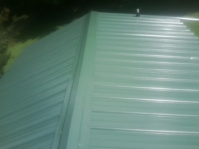 New green metal panels meeting at the ridge of a roof — Flat Roof Repair work by our crew in Jones
