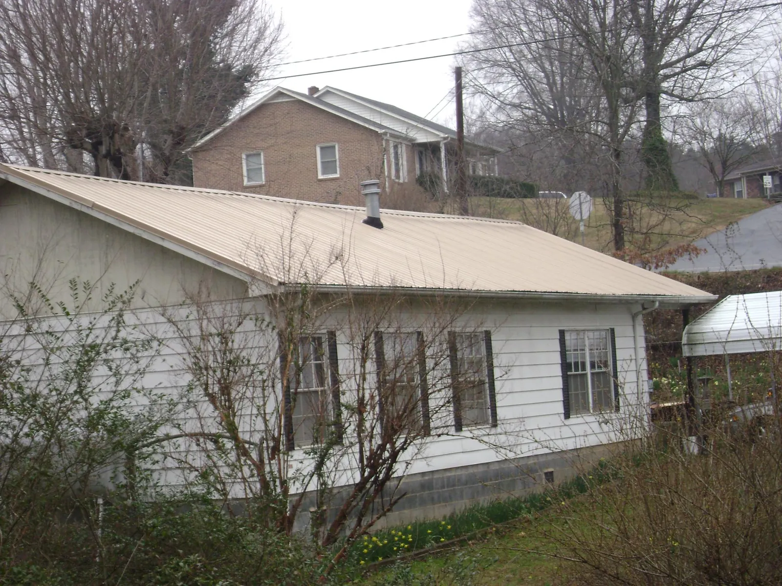 Tan metal roof on a white sided house set into a hillside — Commercial Roofing by Roofing Brothers in Jones