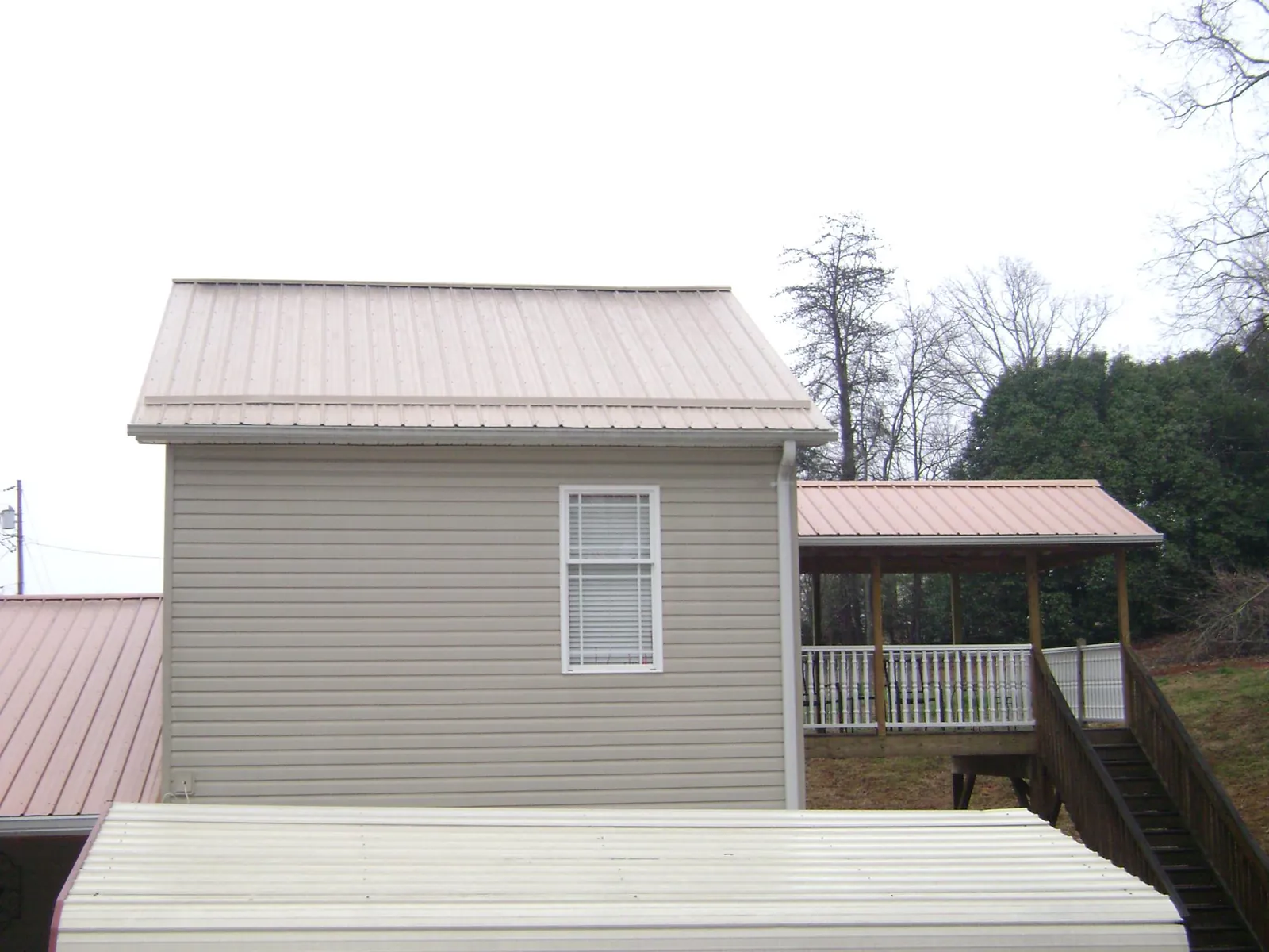Tan metal roofs on a two story addition and attached porch, from a Roof Replacement job in Jones