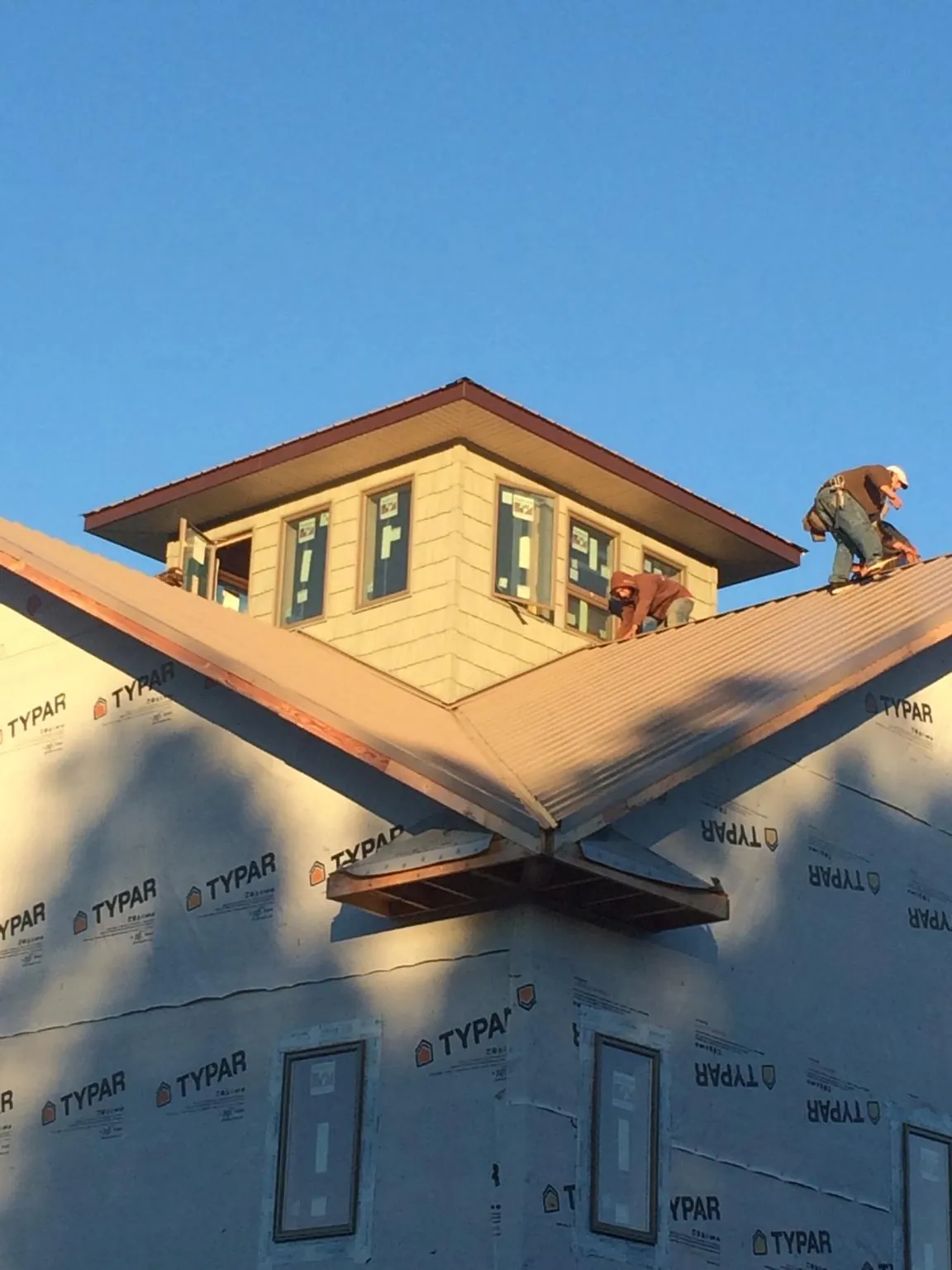 Roofers working around a rooftop cupola on a new metal roof at sunset — Roof Waterproofing in Jones by Roofing Brothers